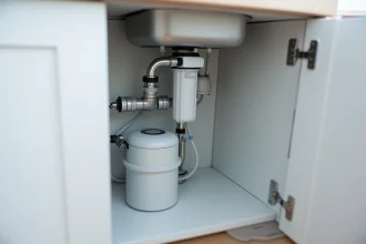 Système de filtration d'eau sous évier avec tuyaux en acier inoxydable et cartouches filtrantes dans un meuble de cuisine moderne